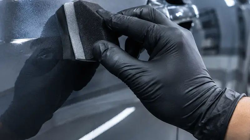 Técnico con guantes negros extendiendo el recubrimiento cerámico sobre la puerta con un bloque aplicador