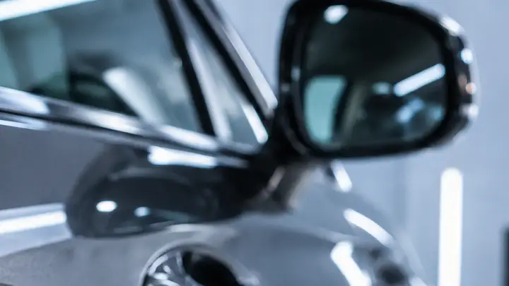 Retrovisor y moldura de la puerta de un coche gris bajo la luz del taller