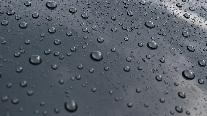 Gotas de agua perladas sobre chapa oscura durante una revisión del recubrimiento